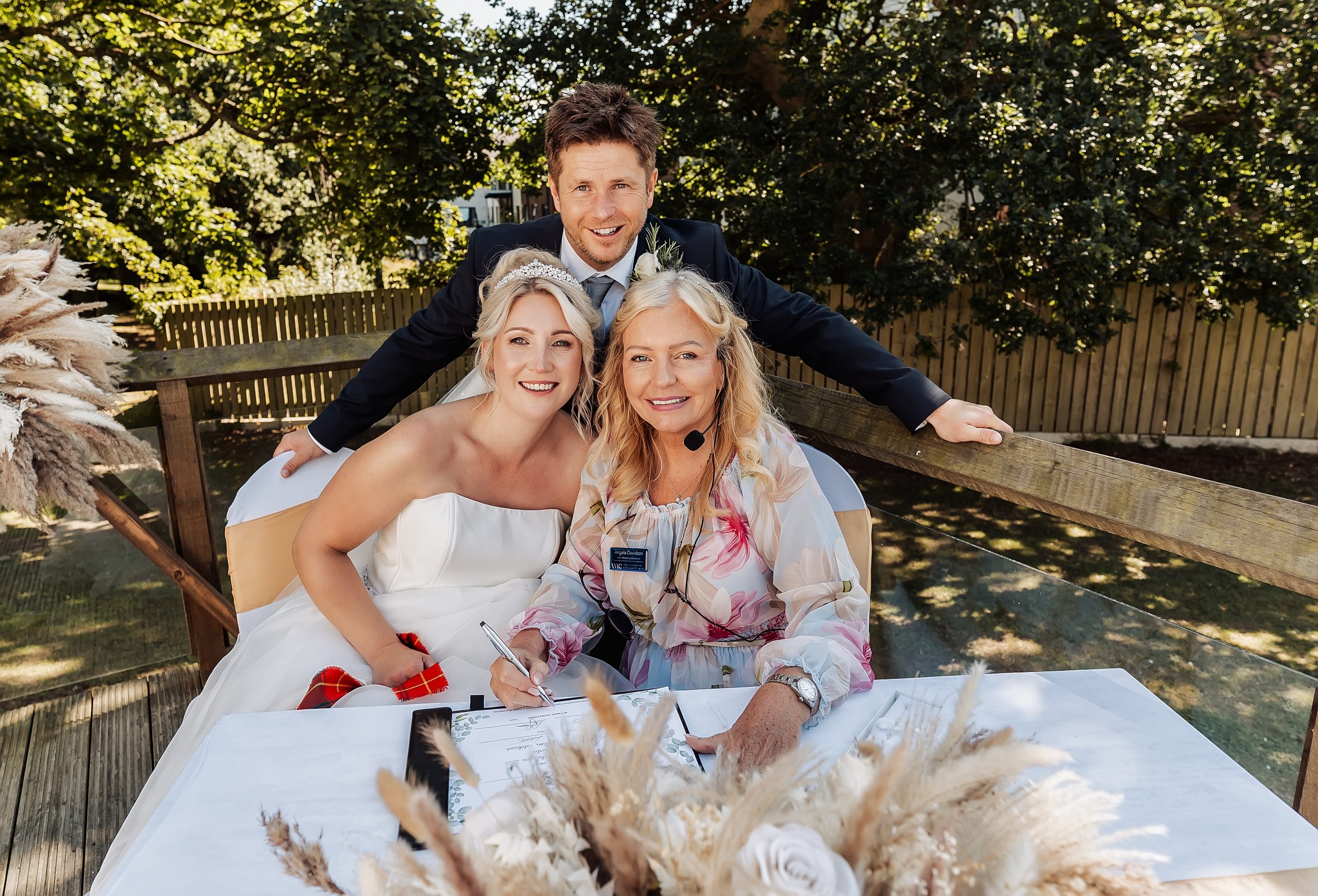 Celebrant sat down and signing the ceremony certificate with the smiling bride and groom